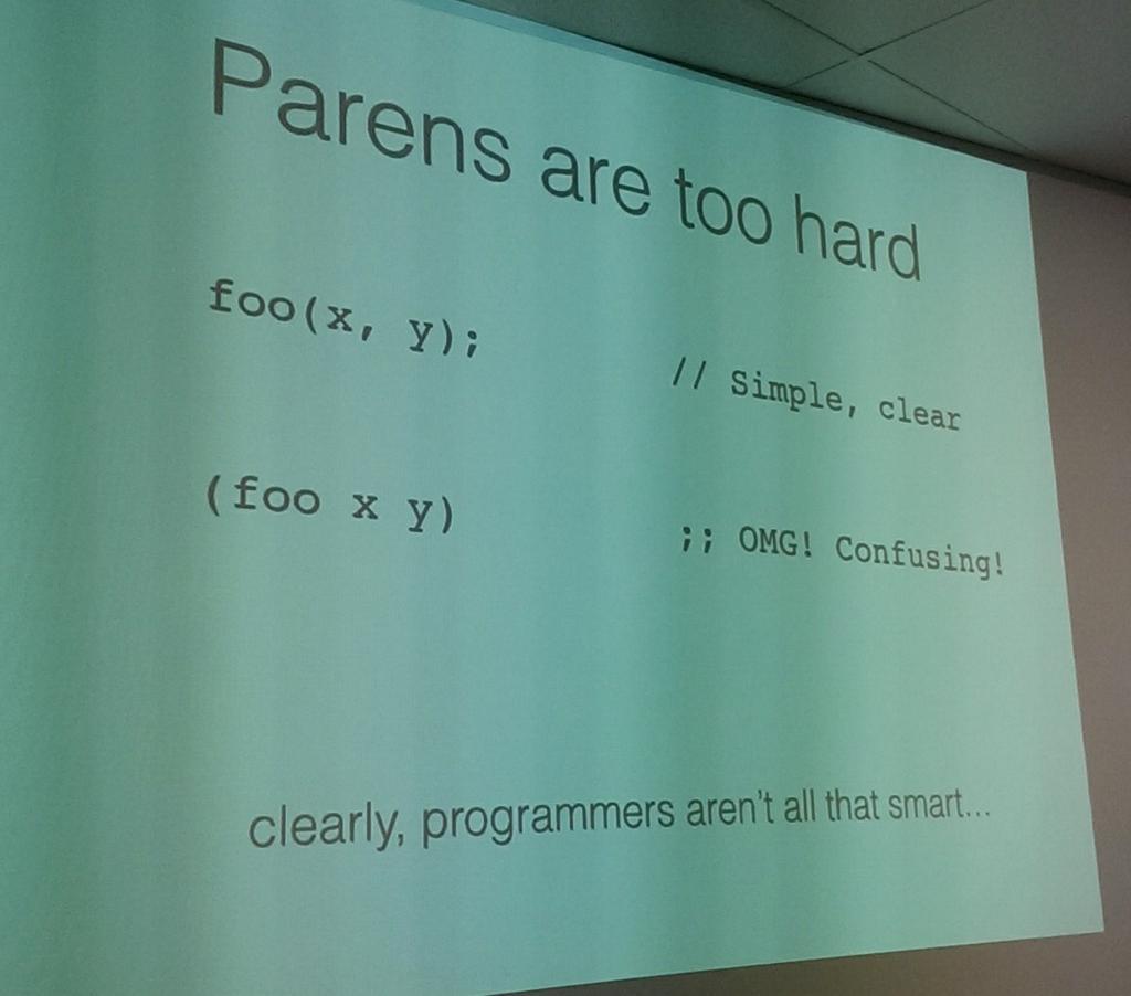 a photo taken at a conference, of a slide that shows function calls as they are in Java or C and as they are in Racket and notes, humorously, that they aren't that different